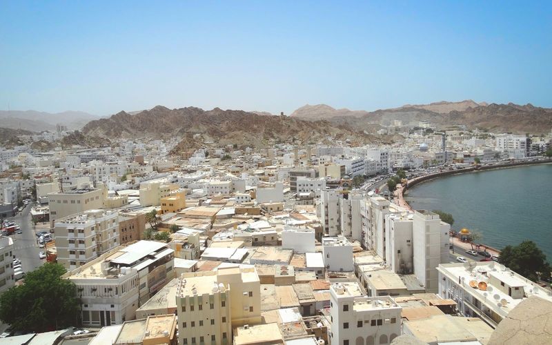 White low-rise buildings of Muscat beside the curving corniche, with rocky mountains behind